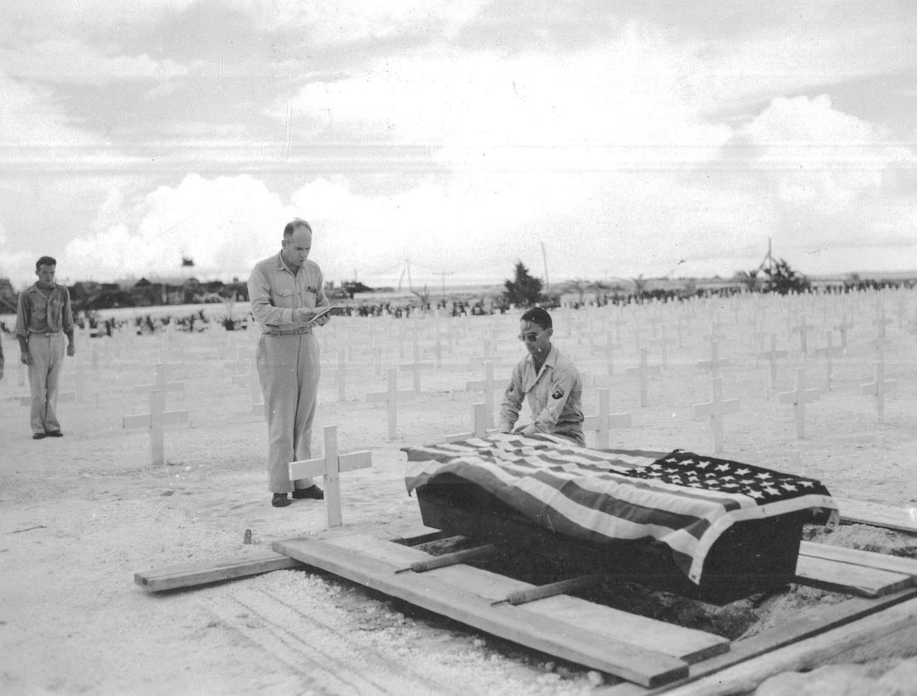 Funeral of one of the four crew who died after rescue, at U.S. Army Forces (USAF) cemetery, Peleliu. C.D. Denham, ChC USNR officiating. 6 August 1945. The remains of all four crew who died after rescue were repatriated to the United States. S2c Ralph Peterson is the only one buried in a national cemetery—Fort Snelling National Cemetery, MN, SECTION C-24, SITE 13541. (National Archives)