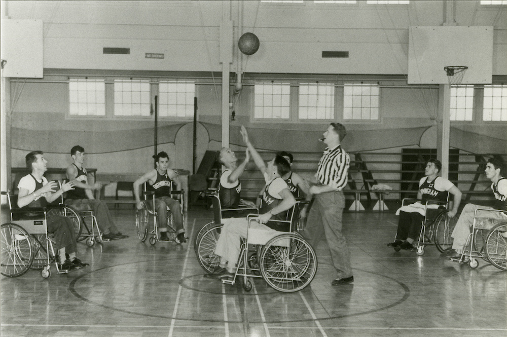Paralyzed World War II Veterans playing a practice game of wheelchair basketball refereed by physical education teacher Robert Rynearson in the gym at the Birmingham VA Hospital in Van Nuys, California, c. 1946. Rynearson created the rules for wheelchair basketball and served as coach and manager of the Birmingham team. (Rynearson Family Archive)