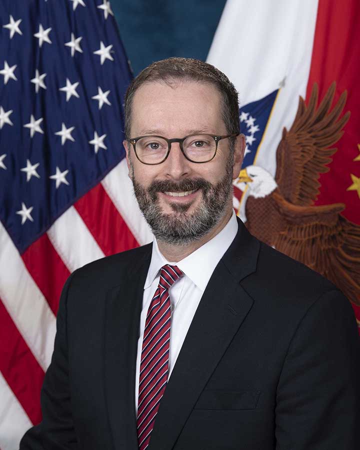 Official image of Joshua Jacobs, sitting in front of the US flag and the Senior Executive Service Flag