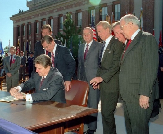 President Reagan signs the Department of Veterans Affairs Act, as Secretary of Defense Frank C. Carlucci, Veterans Administration chief Thomas K. Turnage, and others look on at the National Defense University, Fort McNair, on October 25, 1988. (National Archives)