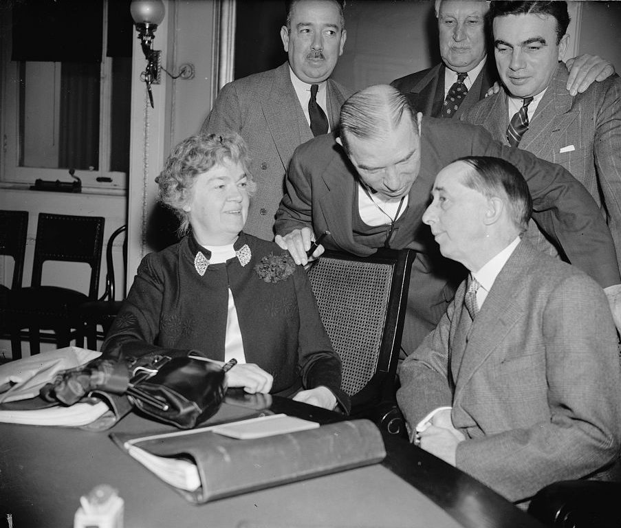 Edith Rogers and other members of the House confer with the American ambassador to Spain over a sensitive report about Spain’s tilt towards Nazi Germany on the eve of World War II. Rogers sits at a table with five other gentlemen in suits around her, one is leaning over to talk to her and Spain's ambassador. (Library of Congress)