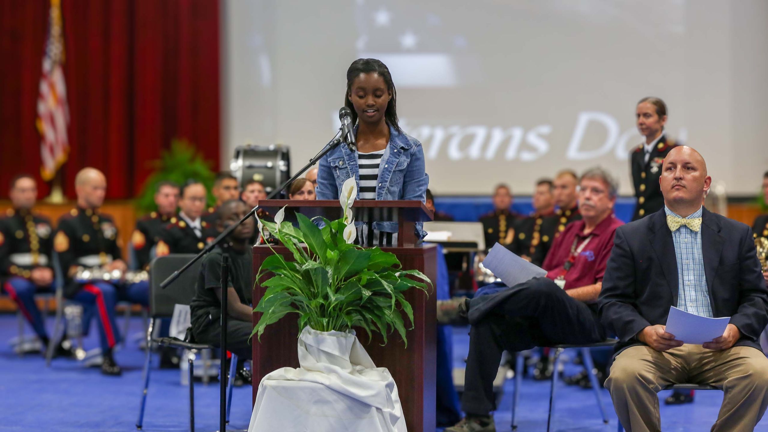 Young person giving a Veterans Day presentation with the Marine band in the background.